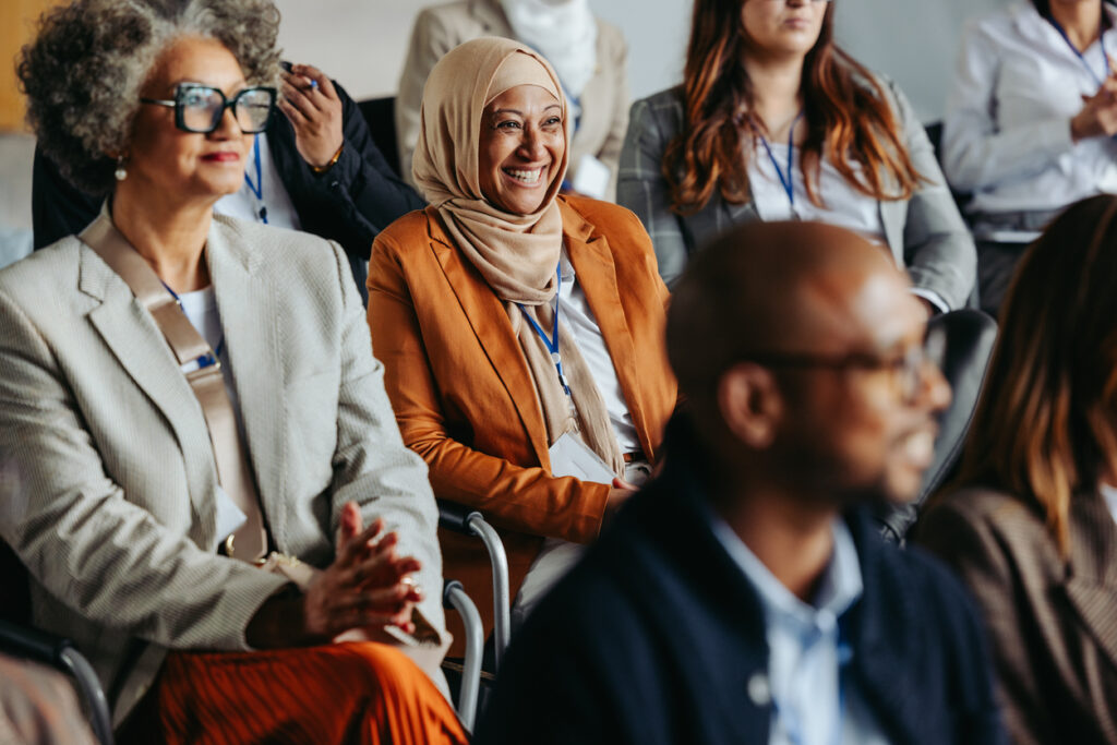 Diverse group of professionals attending a business conference with a Muslim woman smiling in the audience