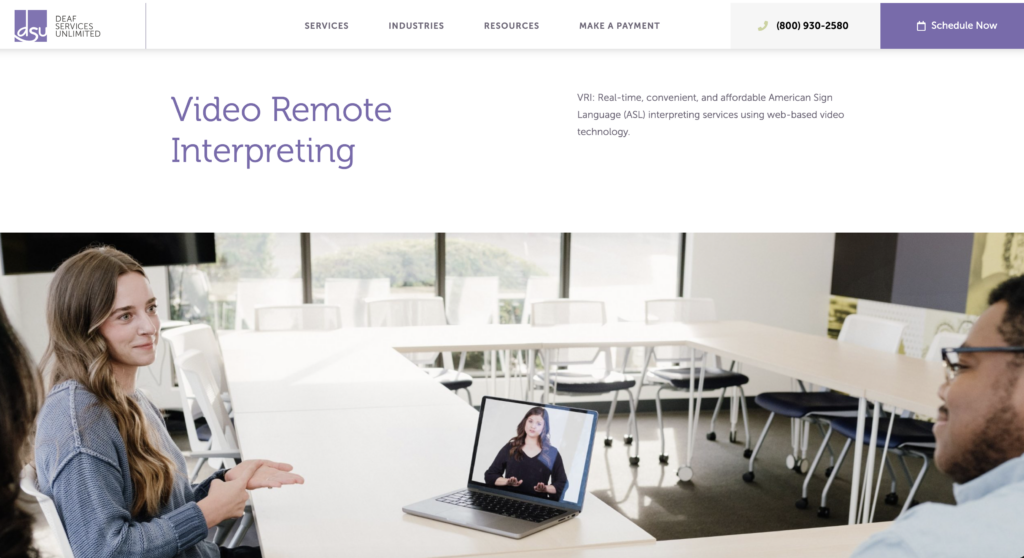 Video Remote Interpreting (VRI) by Deaf Services Unlimited, showing a remote ASL interpreter on a laptop facilitating communication between two people in a meeting room